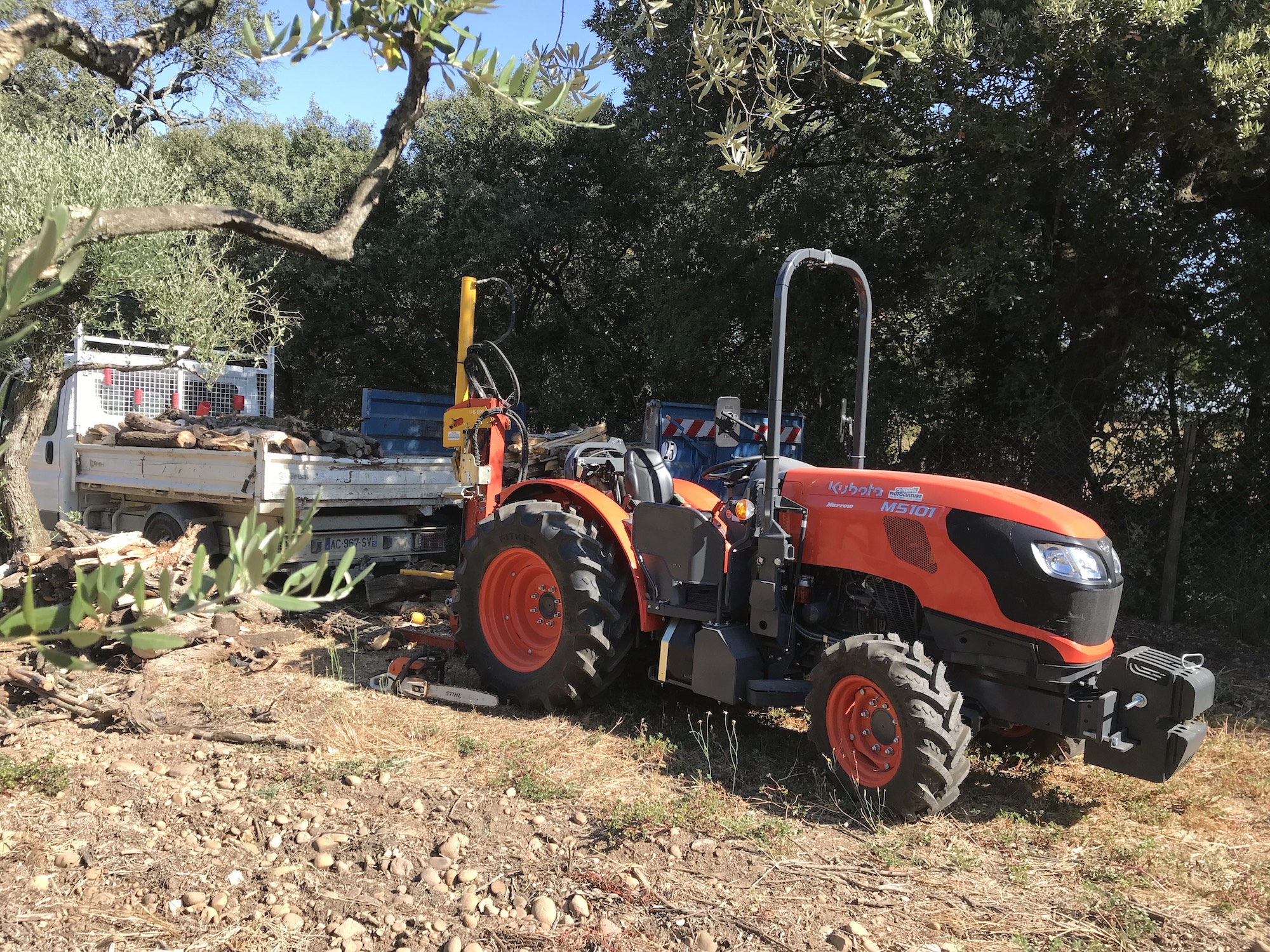Tracteur agricole attelé à une remorque au milieu d'une oliveraie